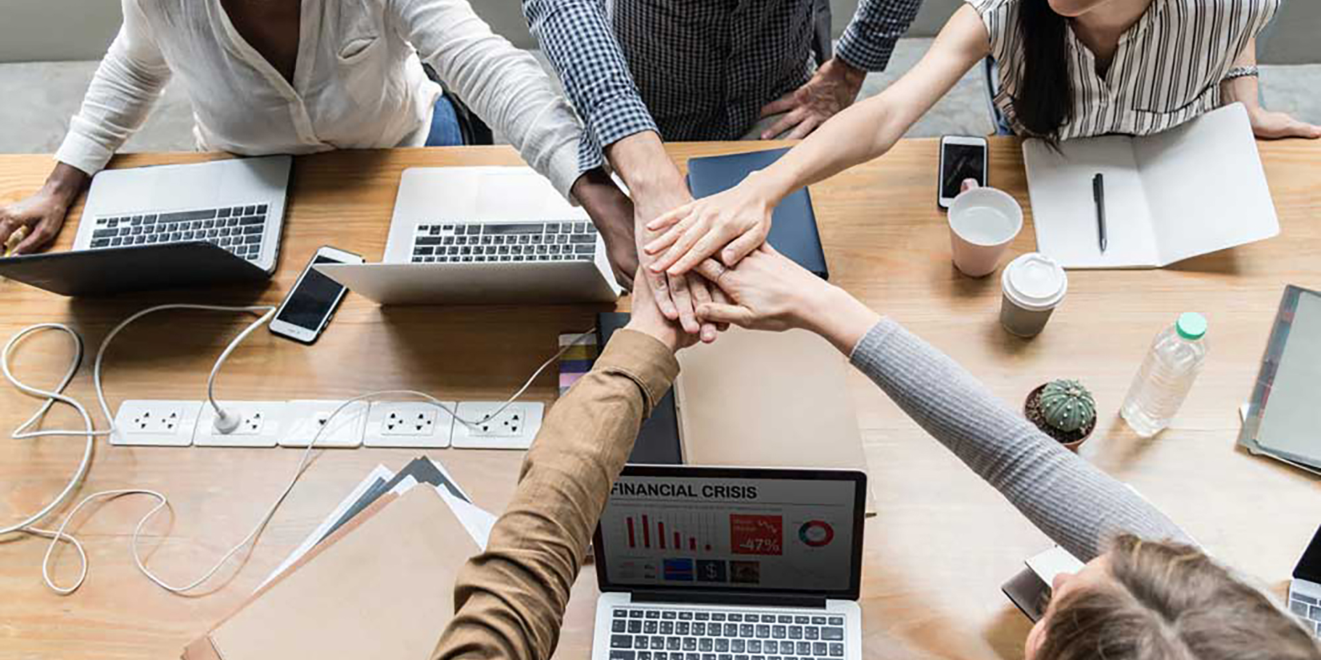 Team stacking hands over laptops in a collaborative office setting